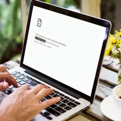 Osoba pracuje na laptopie, na ekranie błąd ERR_SSL_PROTOCOL_ERROR. Obok kawa i kwiaty.