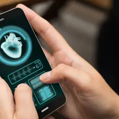 Dłonie trzymają smartfon z aplikacją zdrowie, która pokazuje obraz serca i tętno 67.