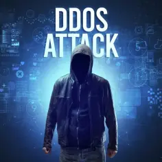 Anonimowa postać w kapturze, symbolizująca atak DDoS, stoi na tle cyfrowych danych i wykresów.