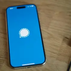 Telefon z niebieskim ekranem i ikoną aplikacji Signal. Obok leży czarny notatnik.