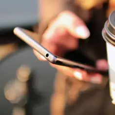 Kobieta trzyma telefon i kubek kawy, szukając informacji, jak doladowac komus telefon Play.