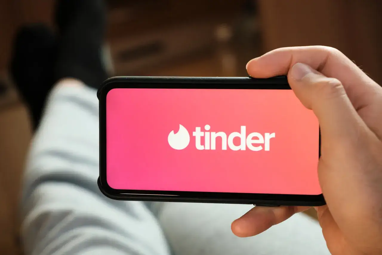Dłoń trzyma smartfon z logo Tindera. Zastanawiasz się, czy tinder jest darmowy? Tak, podstawowa wersja aplikacji jest bezpłatna.