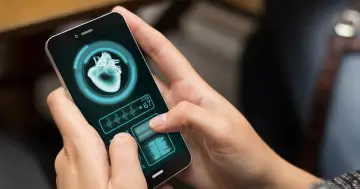 Dłonie trzymają smartfon z aplikacją zdrowie, która pokazuje obraz serca i tętno 67.