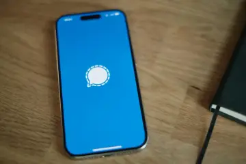 Telefon z niebieskim ekranem i ikoną aplikacji Signal. Obok leży czarny notatnik.
