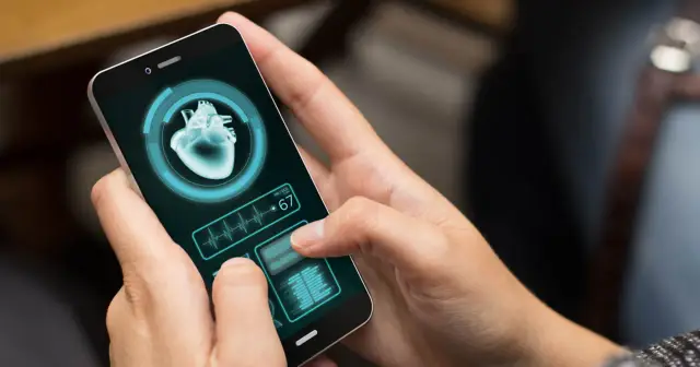 Dłonie trzymają smartfon z aplikacją zdrowie, która pokazuje obraz serca i tętno 67.